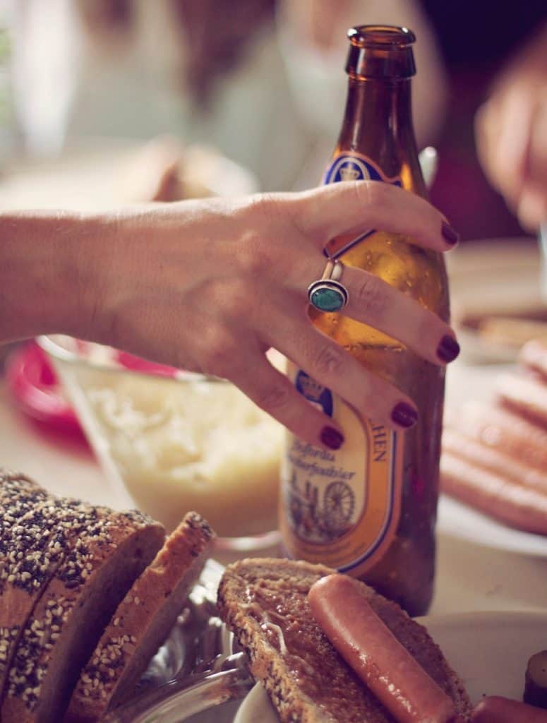 person holding bottle of beer with hotdog in foreground