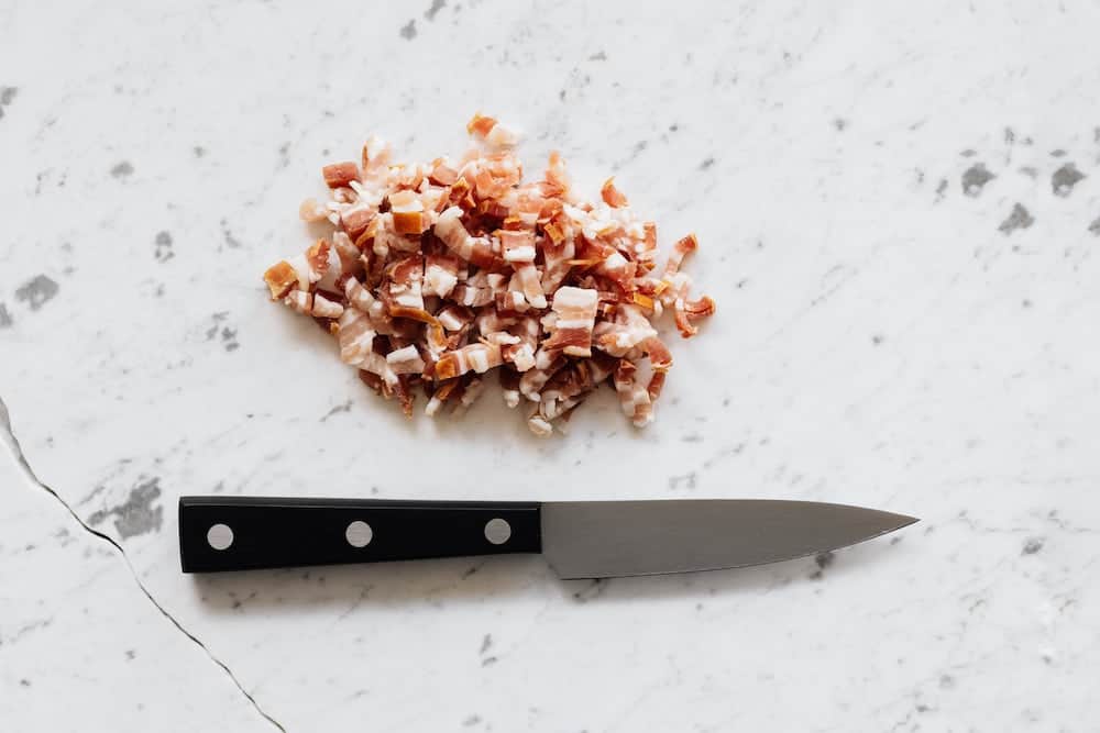 bacon diced into small pieces in a pile next to a knife