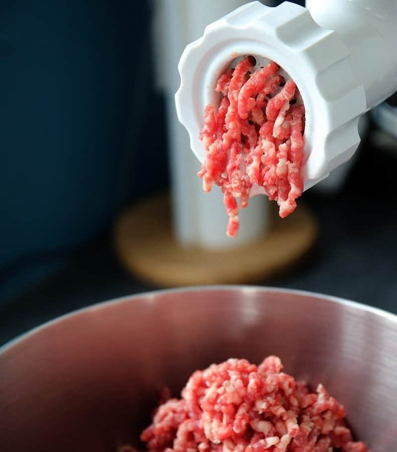 meat grinder grinding meat into steel bowl