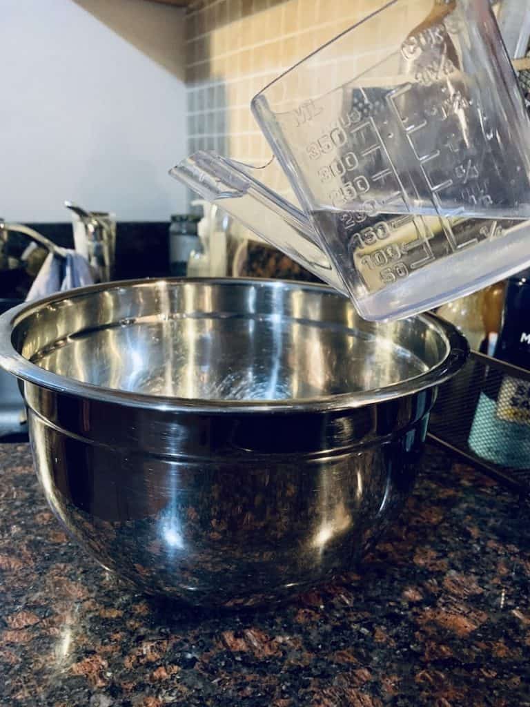 measuring cup pouring water into steel bowl on kitchen counter