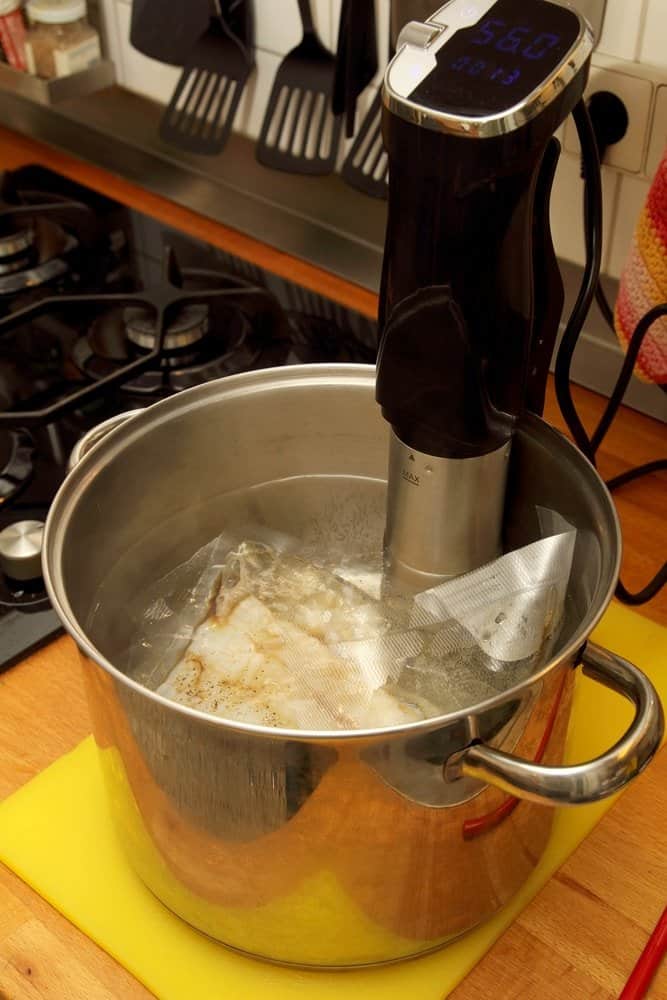 meat in sous vide bag in steel pot with immersion circulator on kitchen counter