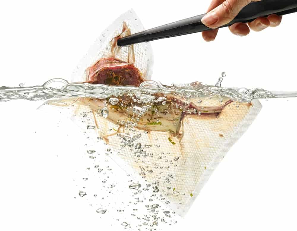 piece of meat in a sous vide bag being lowered into heated water bath