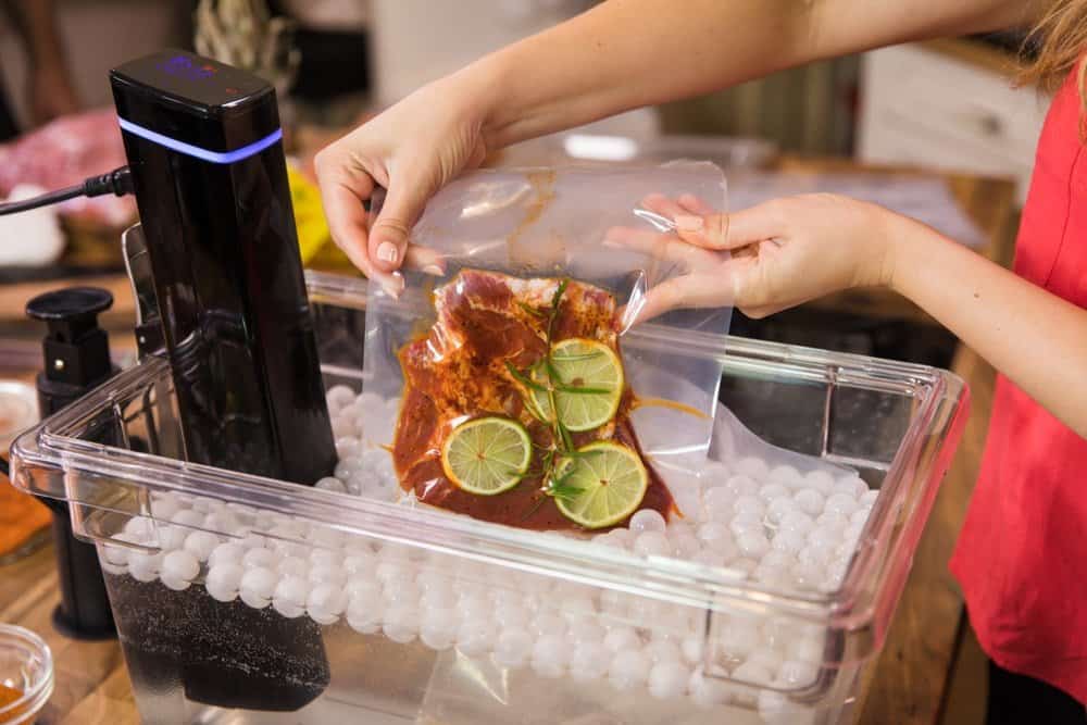 sous vide bag being lowered into sous vide container with ping pong balls and immersion circulator