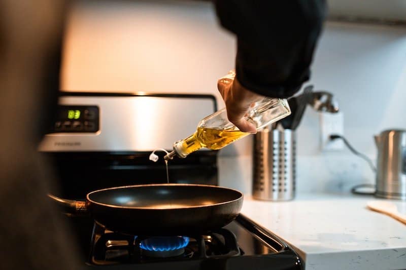 person pouring olive oil in pan on gas stove