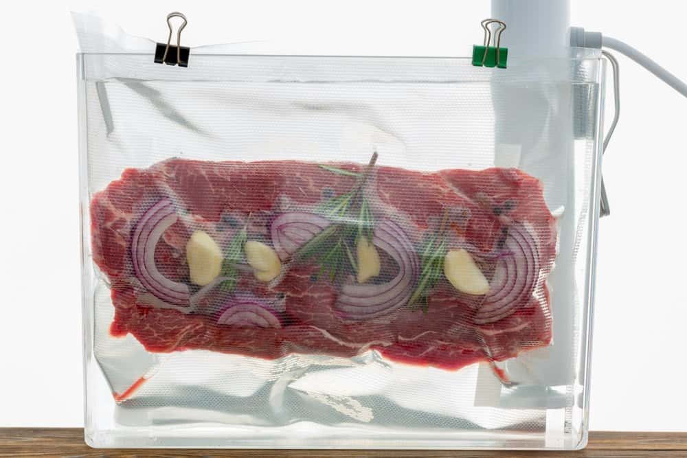 meat in vacuum sealed bag clipped to top of container with sous vide immersion circulator