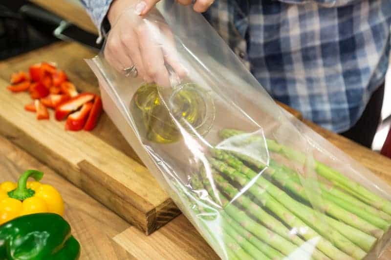 person pouring olive oil into sous vide bag with asparagus