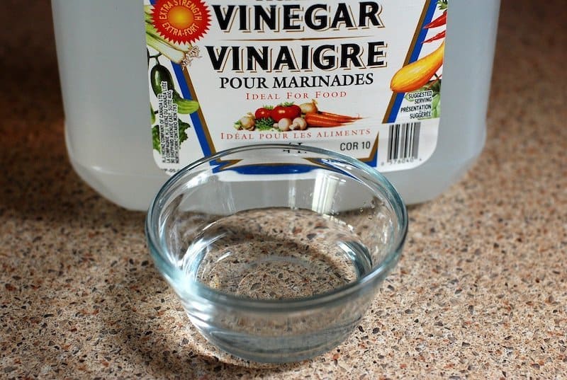 bottle of vinegar with glass bowl of vinegar in front of it