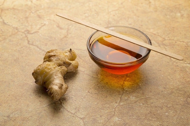 piece of ginger next to small bowl of honey