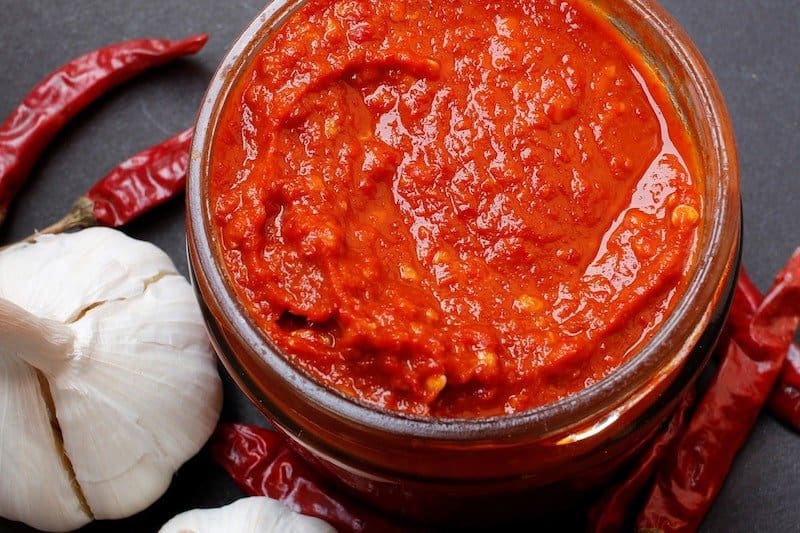 top view jar of hot sauce with chili peppers next to it