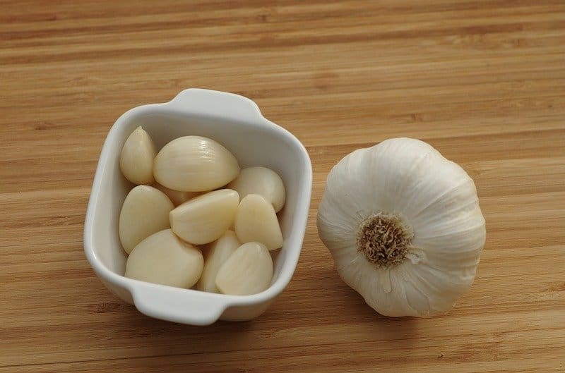 peeled garlic cloves in small white container with whole garlic bulb next to it