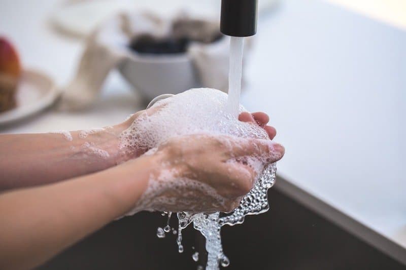 person washing hands at kitchen sink with soap