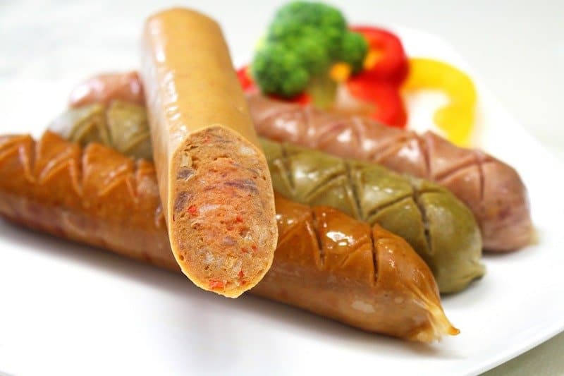 three sausages on a plate with another sausage lying on top sliced down the middle so you can see the inside and casing lining