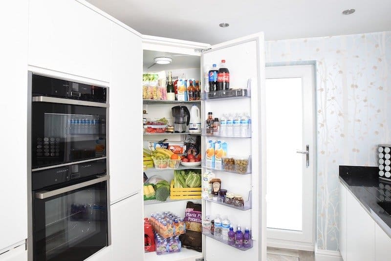 kitchen ovens and fridge with door open and white cabinets