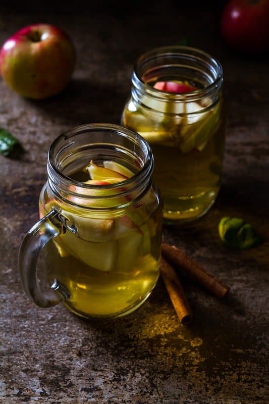 two mason jars will with apple juice with apple slices in them