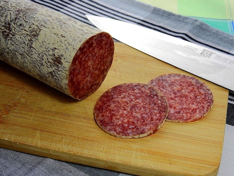 log of salami on cutting board with salami slices next to it