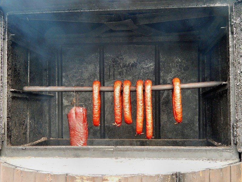 sausage and piece of meat hanging in a smoker