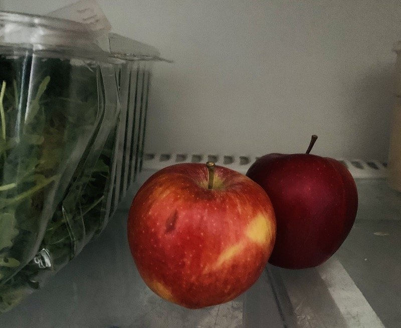 two apples next to salad in a fridge