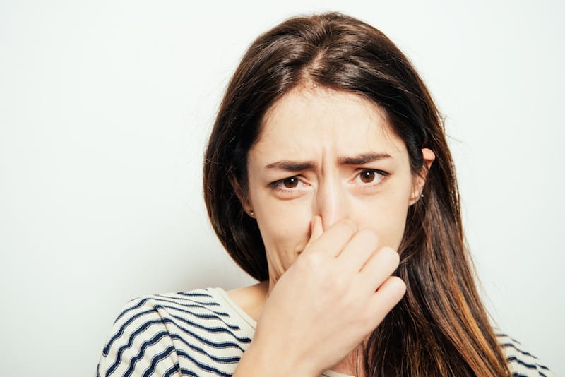 woman with brown hair and striped shirt holding nose due to bad smell