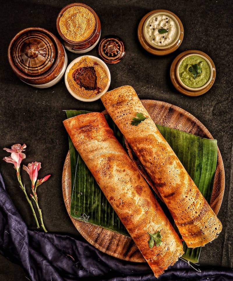 two dosa on plate with small bowls of chutney around it