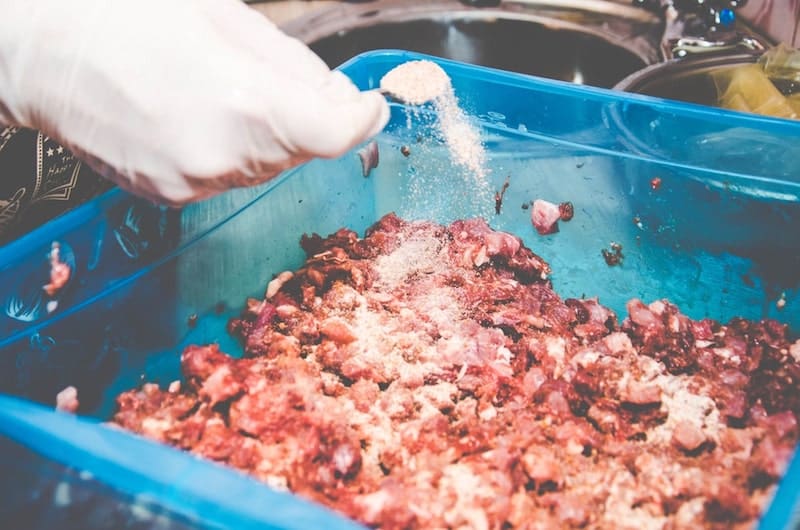 person adding salt to ground meat in plastic container