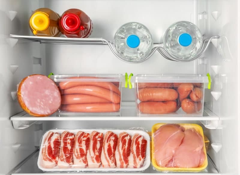 fridge with sausages in containers packaged meat and water bottles