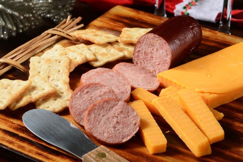 summer sausage on cheese board with sliced cheese and crackers