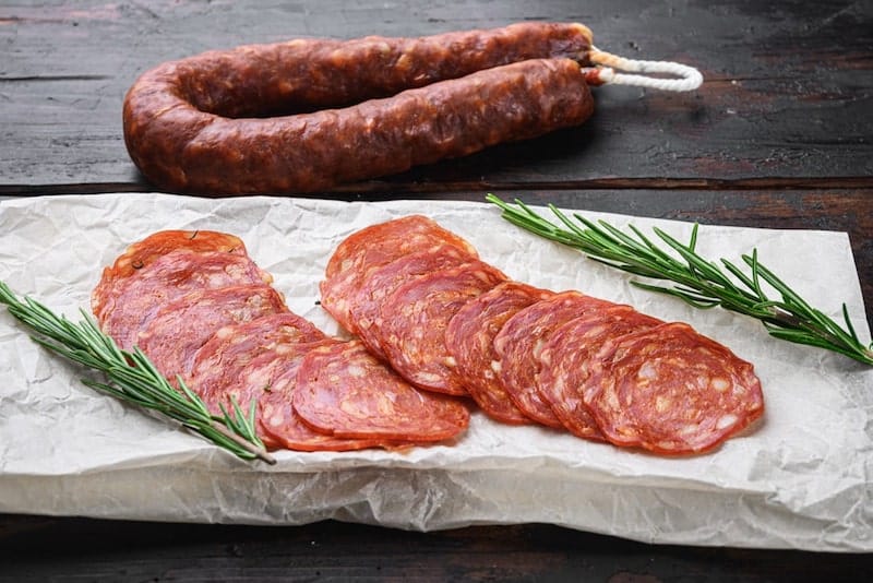 chorizo on string with slices of chorizo on paper with rosemary