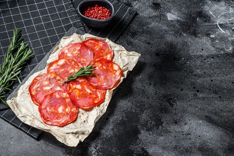 slices of chorizo on paper with rosemary and peppers in background