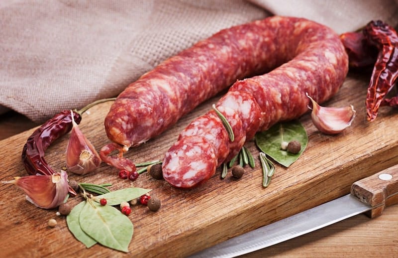 chorizo on cutting board surrounded by spices garlic chili pepper bay leaves peppercorn