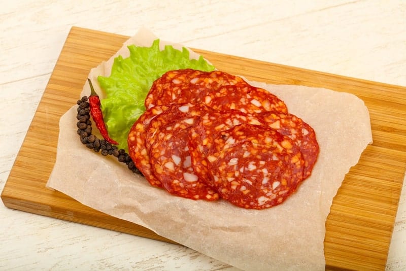 slices of spanish chorizo on cutting board with spices around it