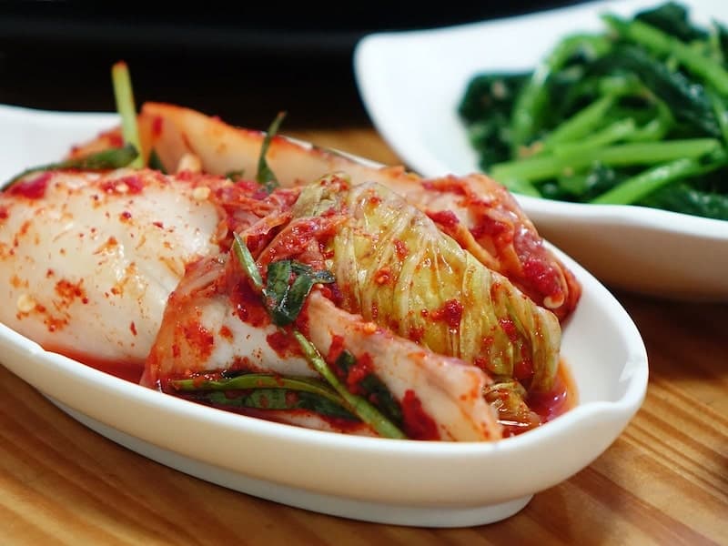 white oval plate with kimchi and plate with vegetables in background