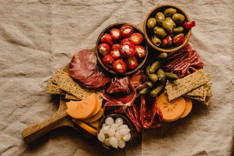 charcuterie board with cheese, prosciutto, pickled onion, olives, crackers, and other cured meats