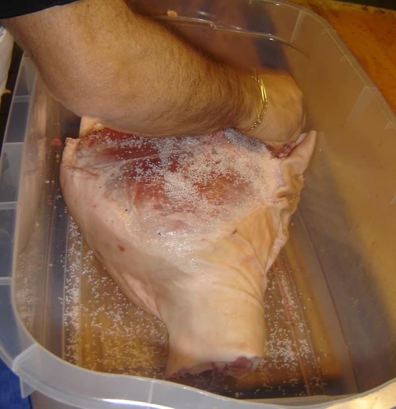 man salting leg of prosciutto in plastic tub