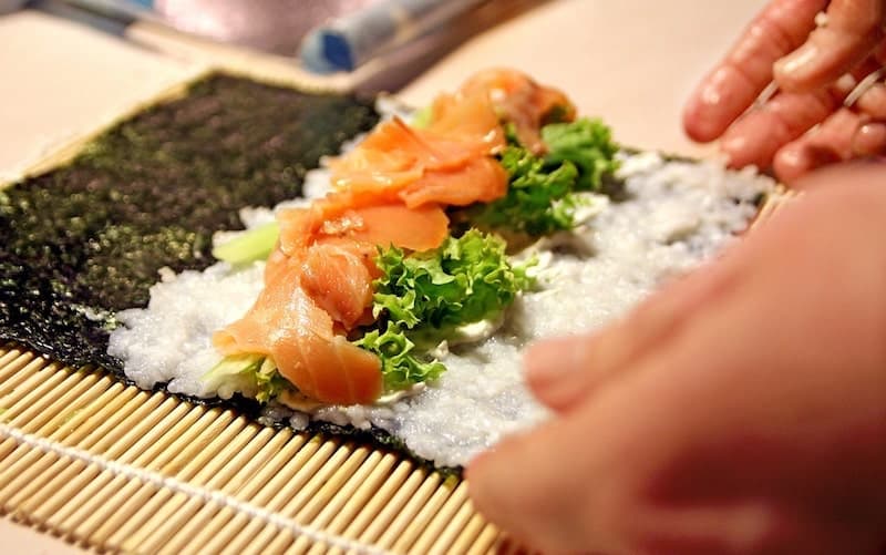 person rolling sushi with bamboo mat