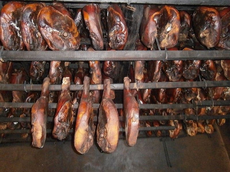 prosciutto legs hanging on drying racks