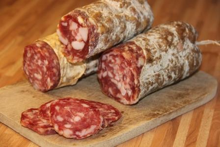 three uncured salami stacked on cutting board with slices next to it