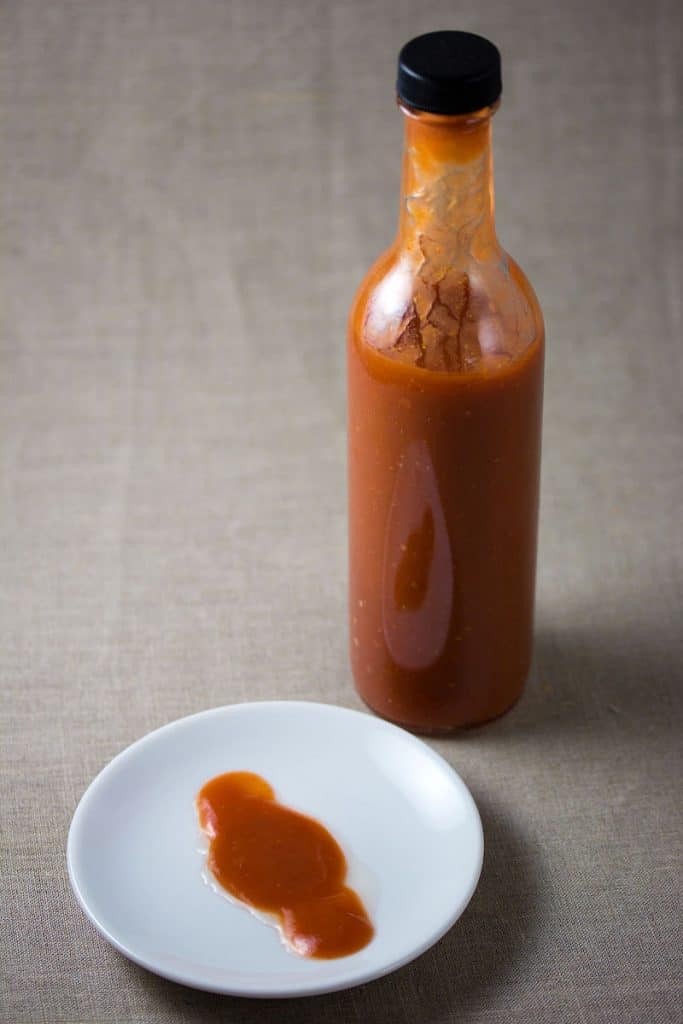 bottle of fermented hot sauce with white place next to it with some hot sauce poured out onto it