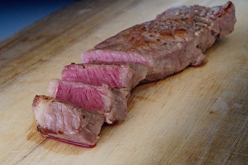 sous vide steak cut in slices on chopping board show pink inside no gradient