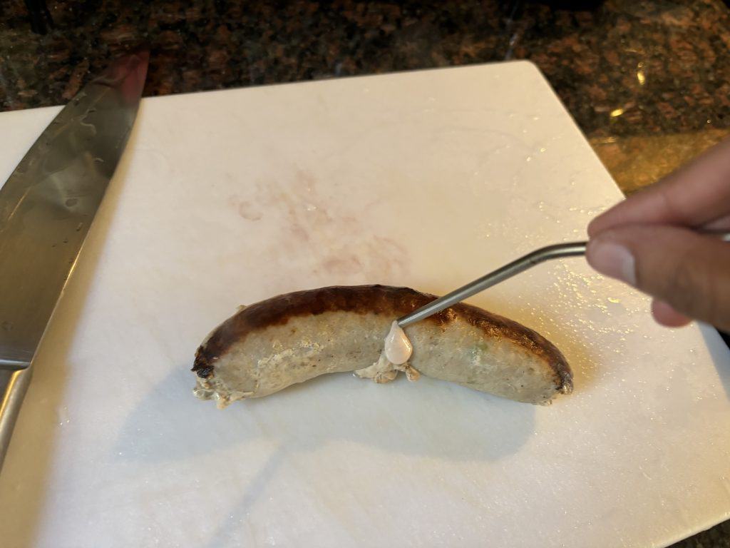 inserting thermometer probe into center of sausage to read temperature