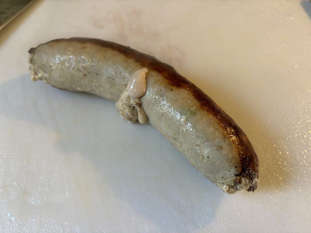 sausage resting on cutting board with juices leaking from casing